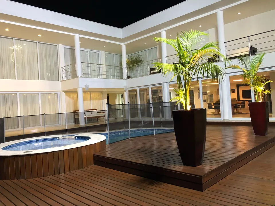 Área externa com deck, piscina e palmeiras iluminadas